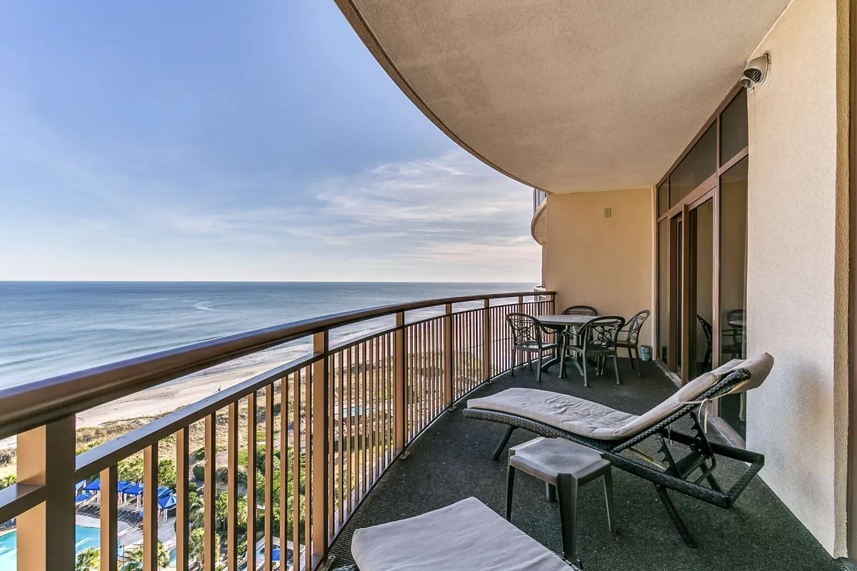 A tranquil balcony with comfortable furniture and a curved railing overlooking the ocean. The scene is serene, with a picturesque sunrise or sunset view, creating the perfect backdrop for morning coffee or winding down with the sound of the waves.