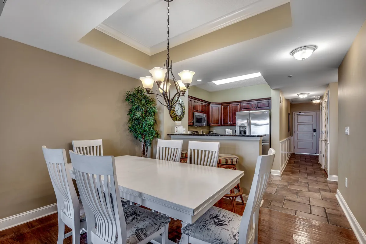 A bright dining area with a welcoming dining table, elegant chandelier, and a direct view into the kitchen area. Decorative plants add a touch of warmth, and the setup is perfect for leisurely brunches or family meals. The atmosphere is warm and communal, enhancing the sense of togetherness.