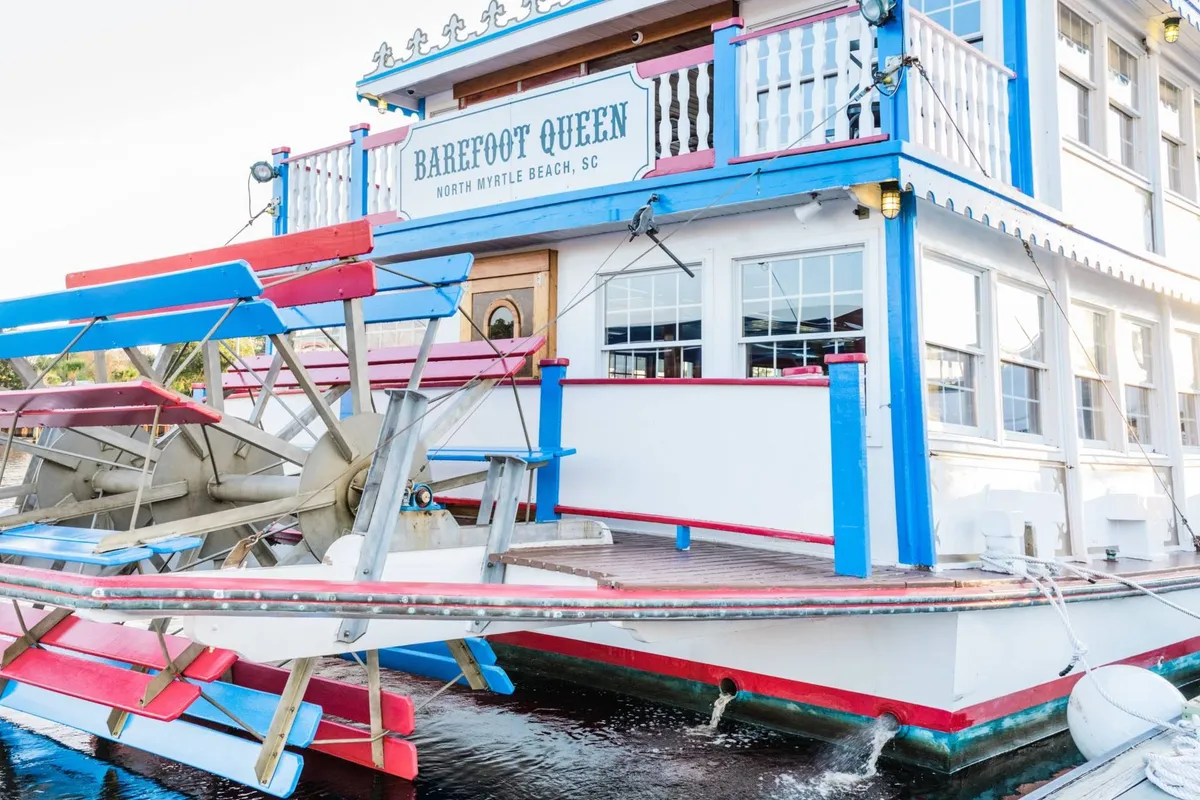 A vibrant waterside view of the Barefoot Queen paddlewheel boat docked near a colorful facade. The scene captures the playful, social side of the local area, with hints of sunset lighting and signage that invite exploration. The mood is relaxed and cheerful, perfect for couples seeking memorable experiences just steps from the resort.