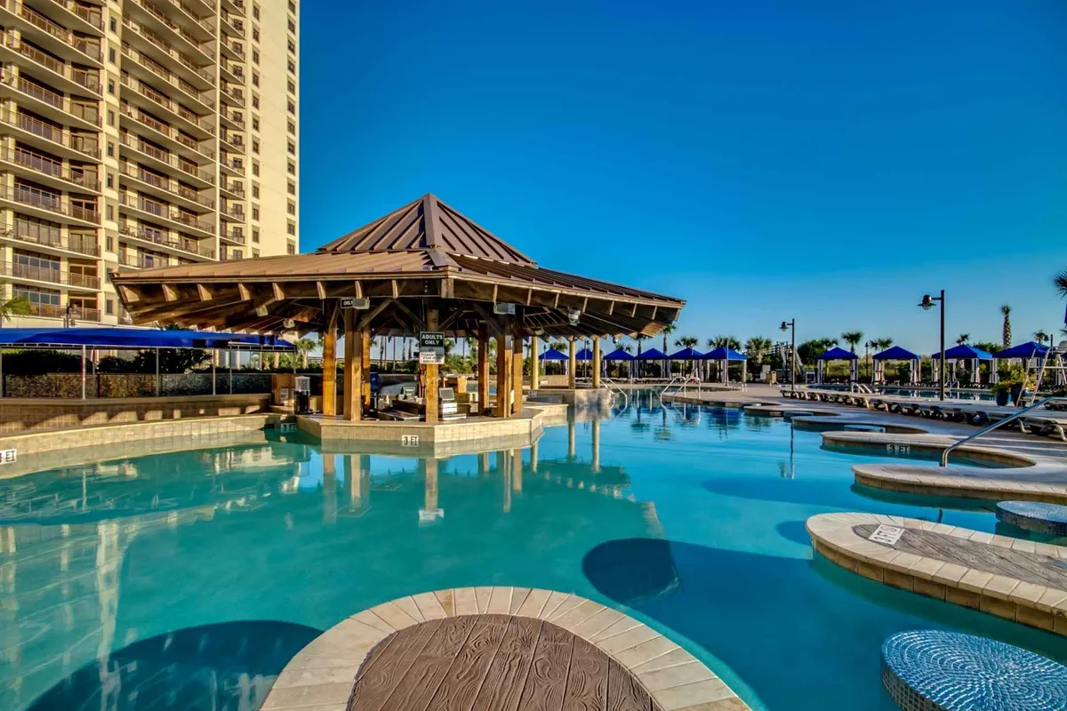 This image displays a vibrant pool area framed by cabanas and lounge chairs, with palm trees providing a tropical backdrop. Guests are seen swimming, sunbathing, socializing, and enjoying refreshing drinks at the poolside cabana, all under a warm, inviting light that hints at sunset leisure.